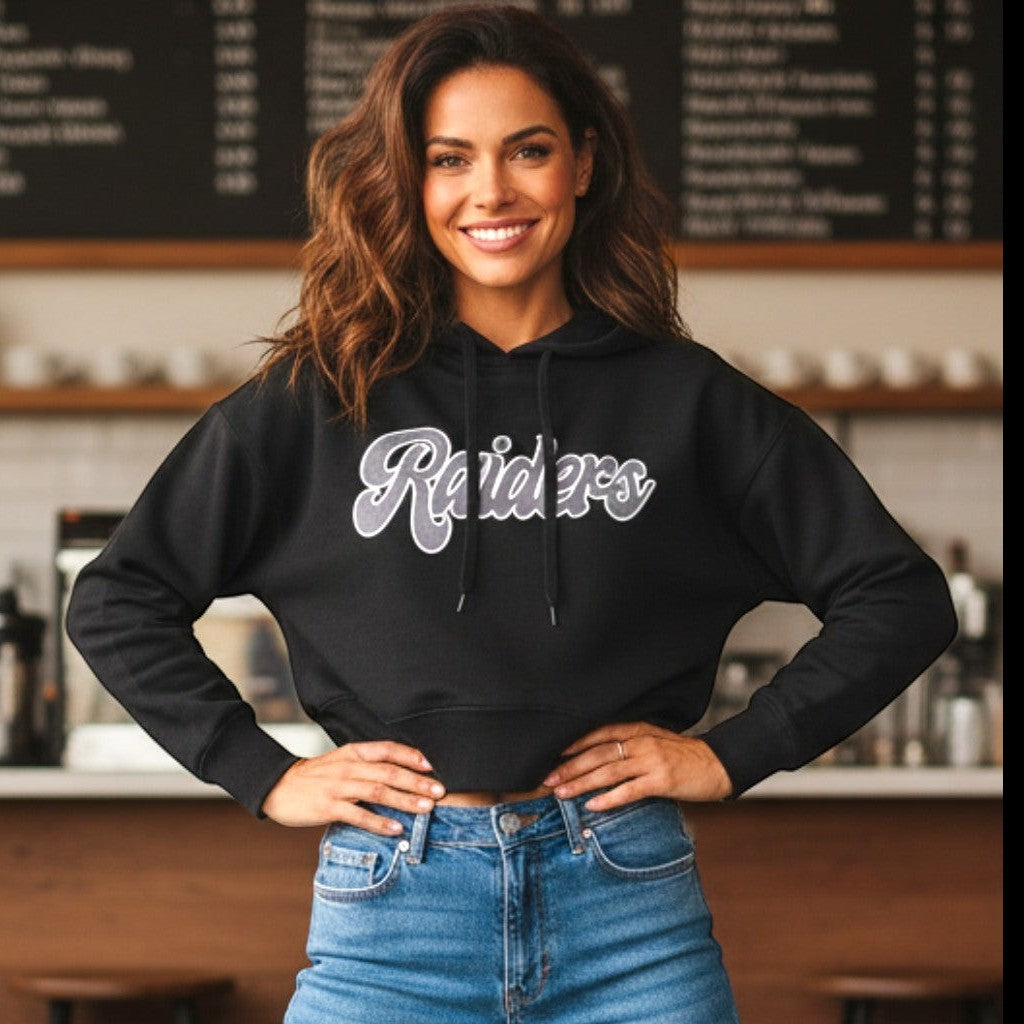 Coliseum Sports women's black cropped Las Vegas Raiders pullover hoodie with script graphic worn by a smiling woman